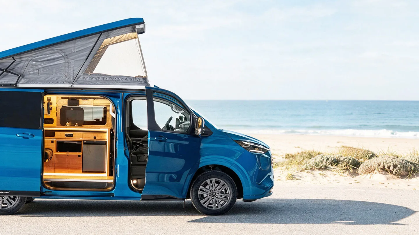 blauer Campervan mit Dachzelt am Strand 
