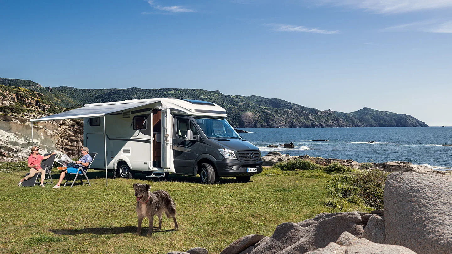 Wohnmobil steht auf grüner Wiese am Meer und hat eine Markise ausgefahren 