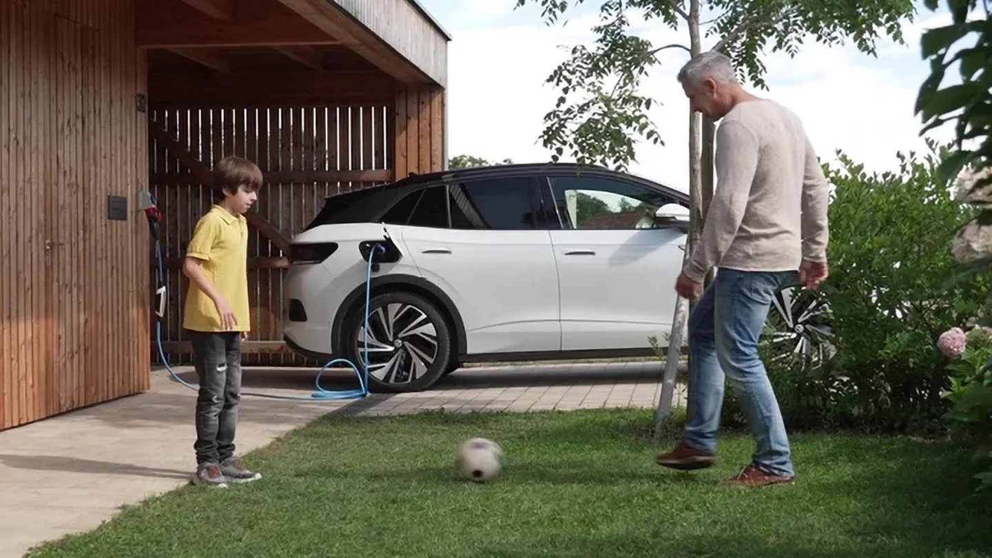 Ein Vater spielt mit seinem Sohn Fußball im Garten während das E-Auto der Familie mit der mobilen Wallbox geladen wird.