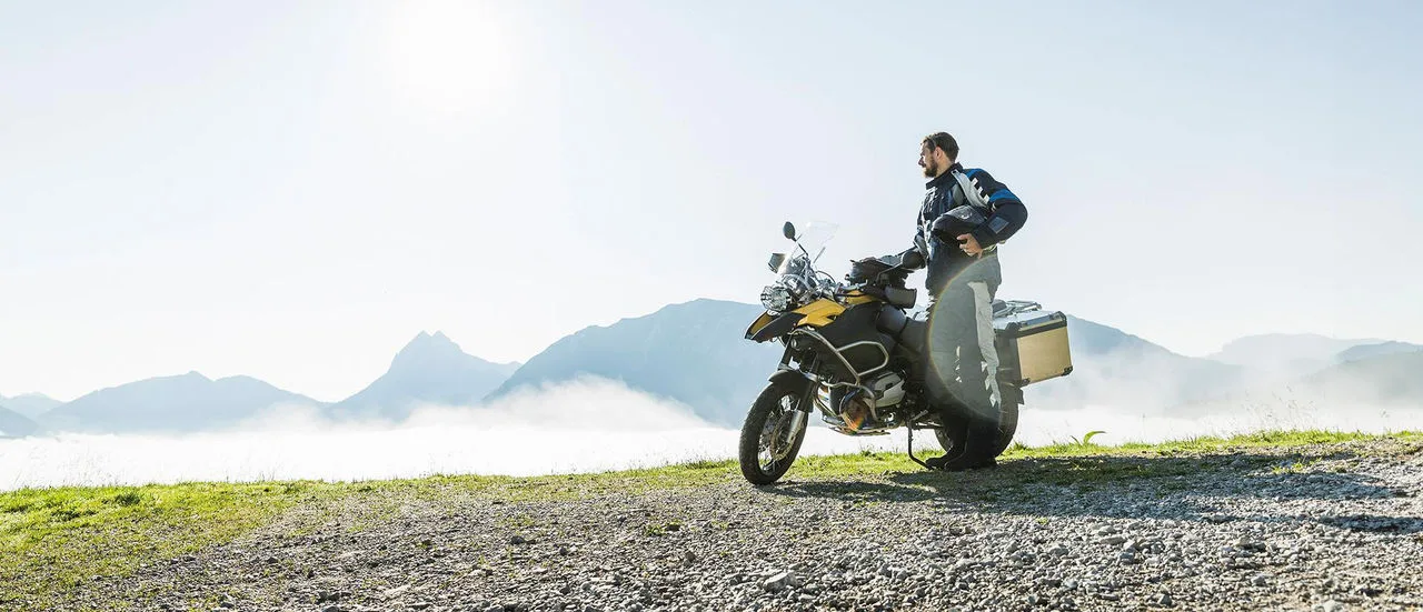 Mann steht in voller Motorradbekleidung neben seinem Motorrad