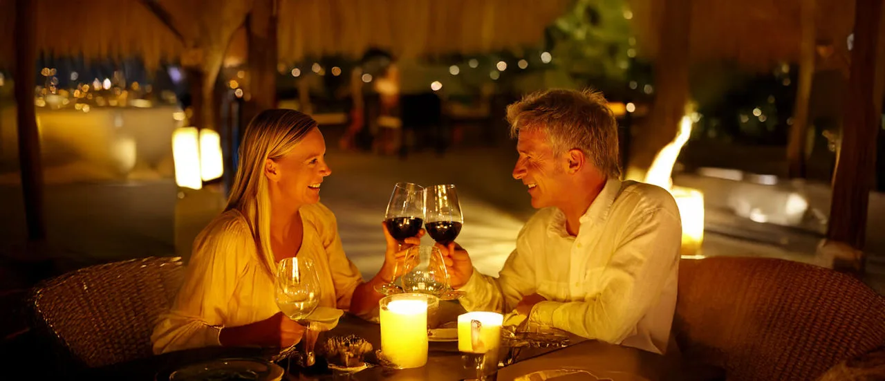 Ein Paar sitzt bei Kerzenschein an einem Tisch im Restaurant und stößt mit Wein an.