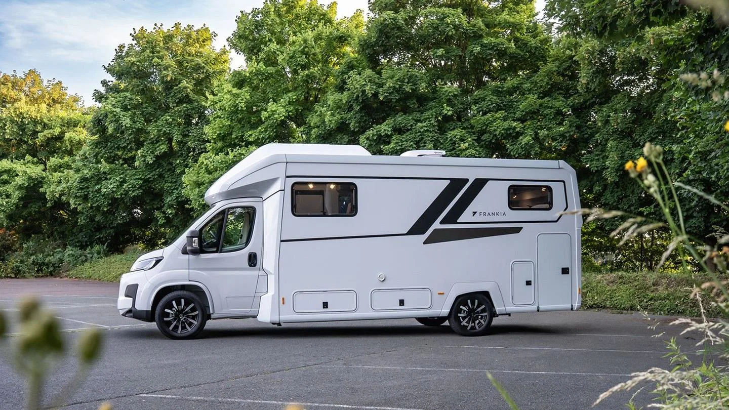 Wohnmobil steht auf einem Parkplatz im Grünen