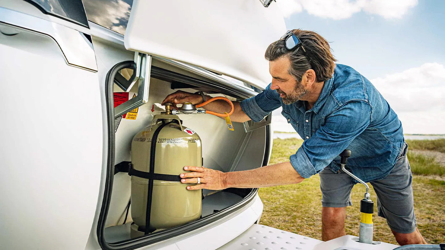 Mann mit Gasflasche am Wohnwagen 