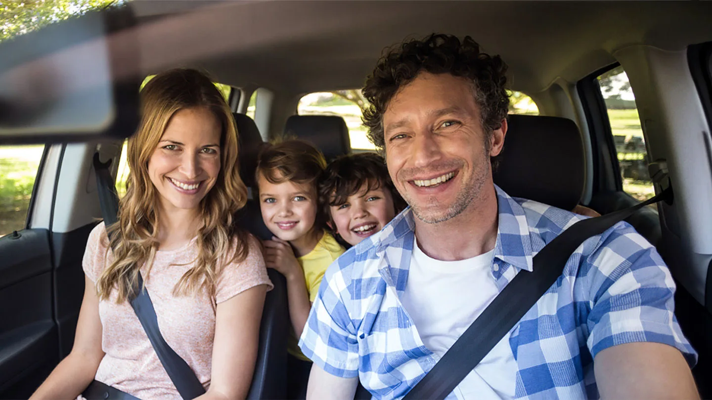 Eine Familie im Auto mit zwei Kindern, alle lachen