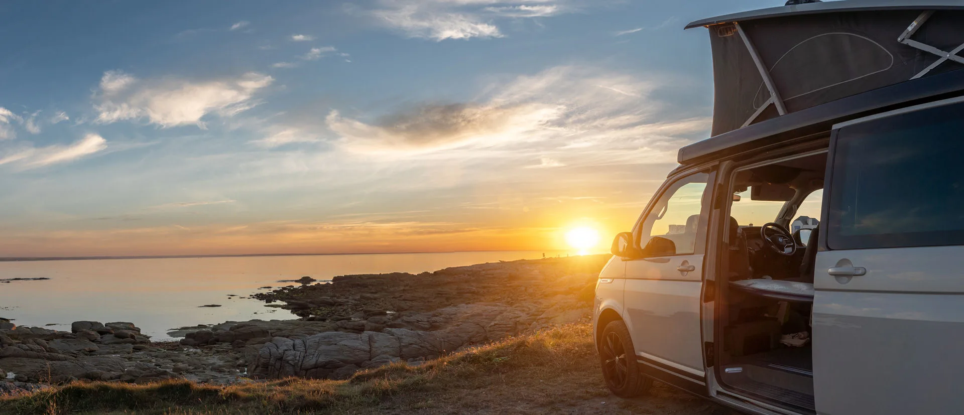 Campervan mit Aufstelldach am Strand bei Sonnenuntergang
