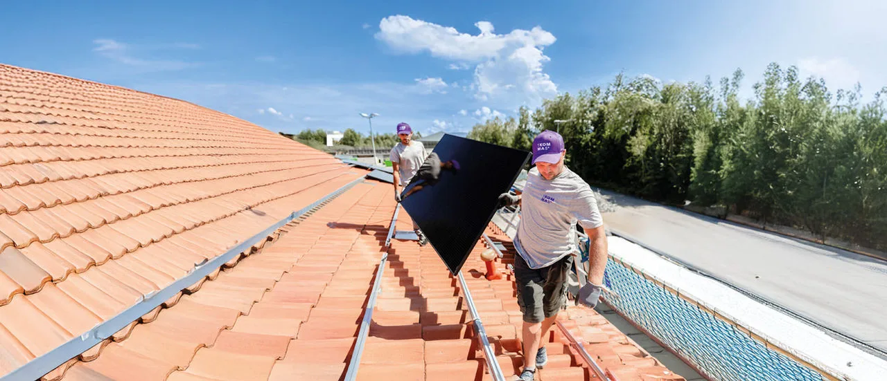Handwerker von 1KOMMA5° montieren eine Photovoltaik Anlage auf ein Hausdach.