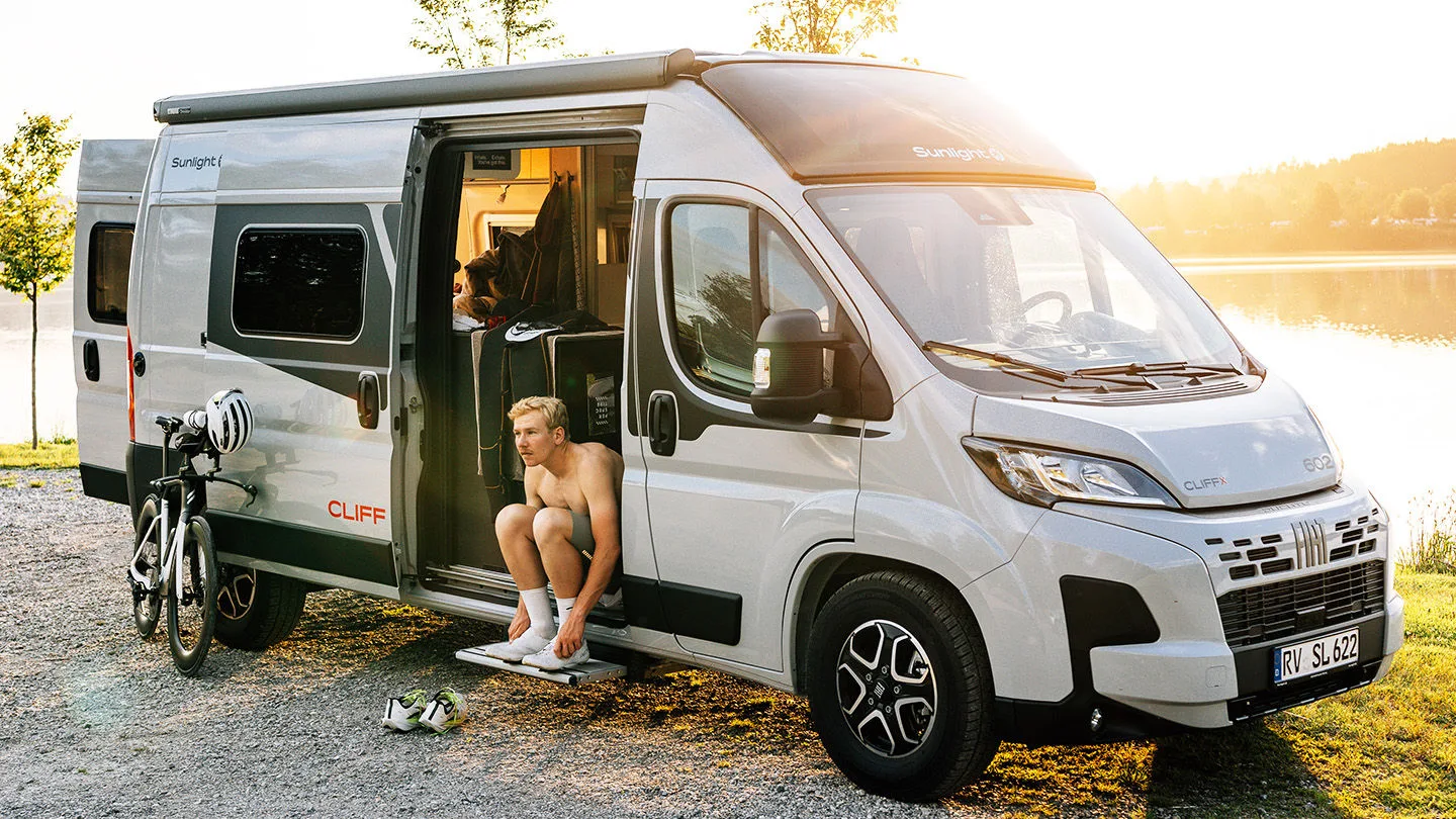 Sunlight Camper steht an einem See und ein Mann macht sich fertig zum Rennrad fahren