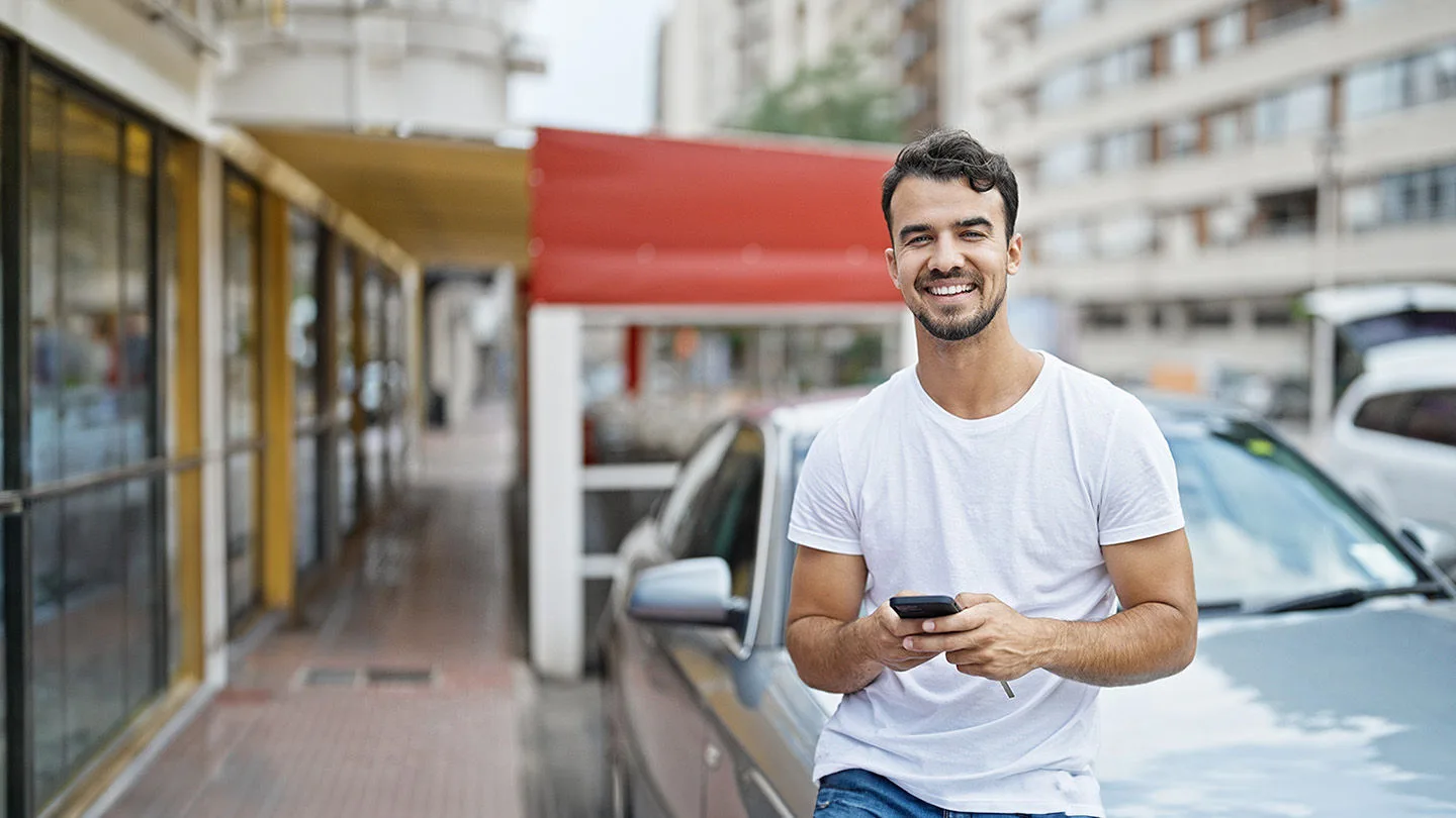 Mann steht vor einem Auto mit dem Handy
