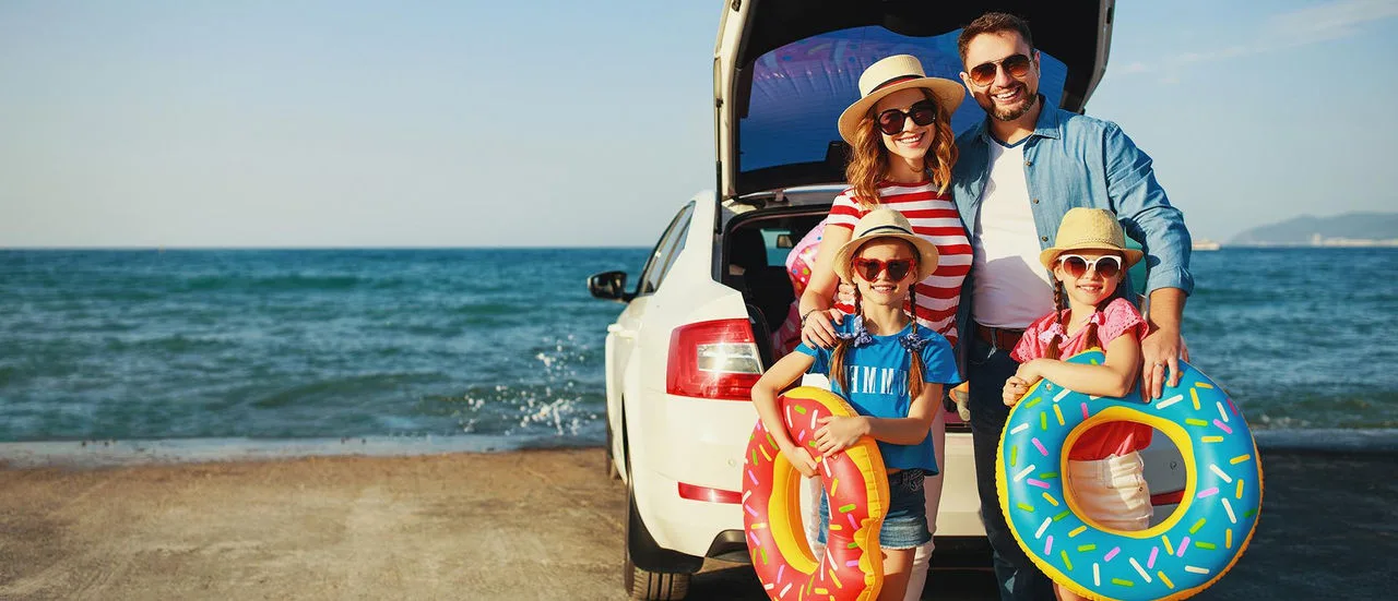 Familie im Sommer am Meer hinter einem Auto
