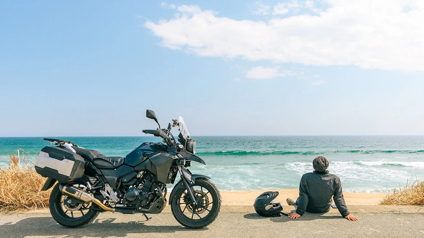 Mann mit Motorrad sitzt an einem Strand