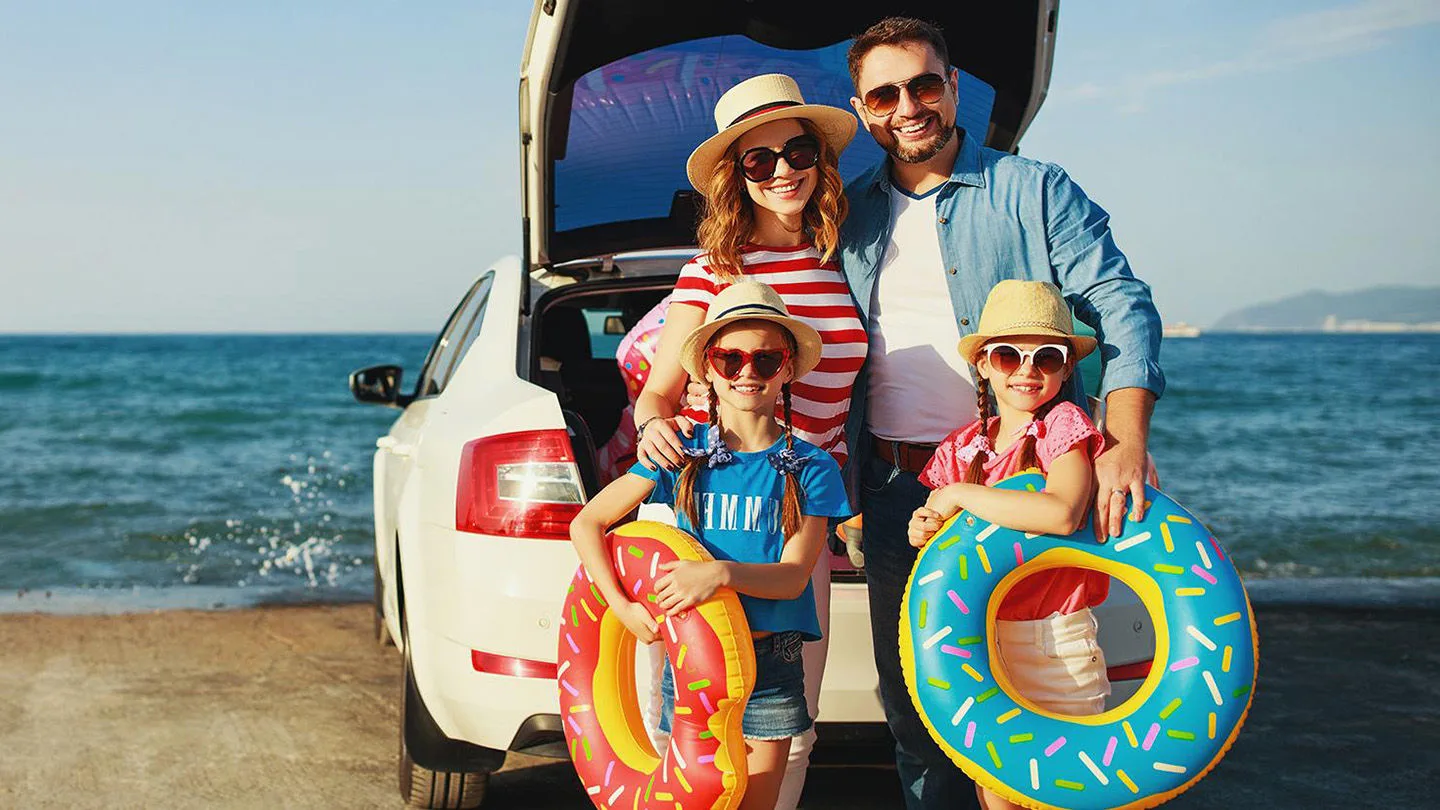 Familie im Sommer am Meer hinter einem Auto