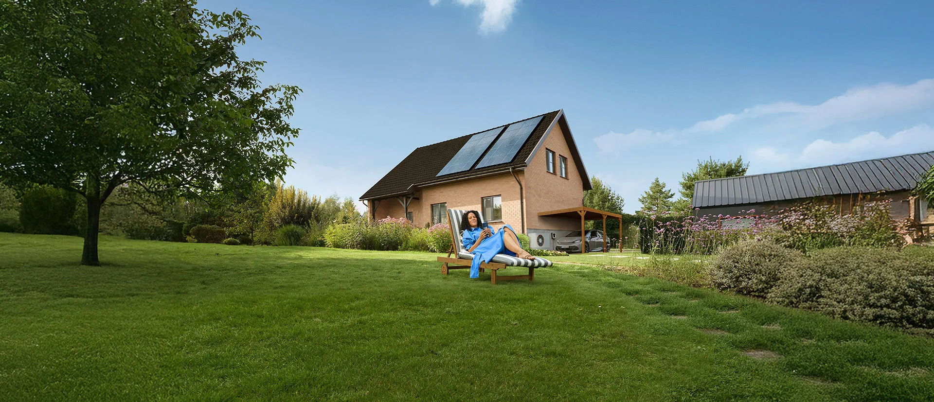 Eine Frau liegt entspannt auf der Liege in ihrem Garten vor dem Haus weil sie mit dem Stromtarif der EnBW günstigen Strom hat.