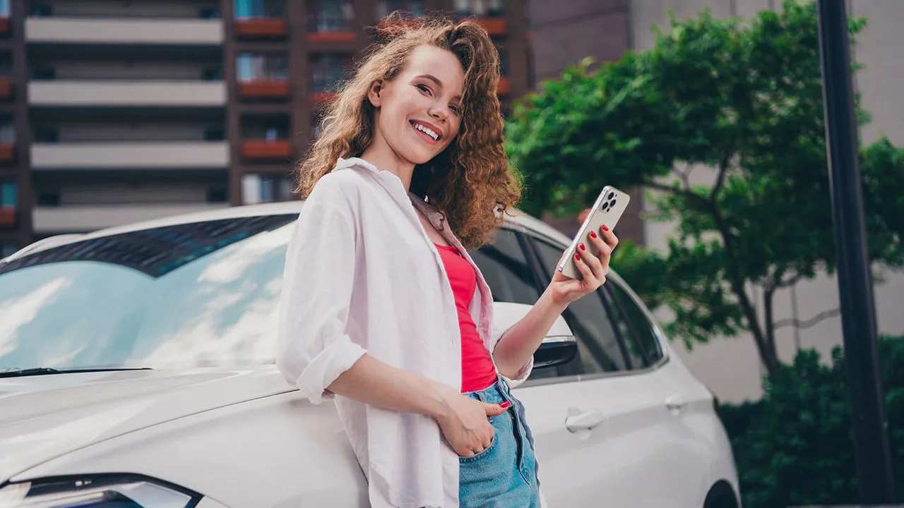 Frau steht am Auto mit einem Handy in der Hand