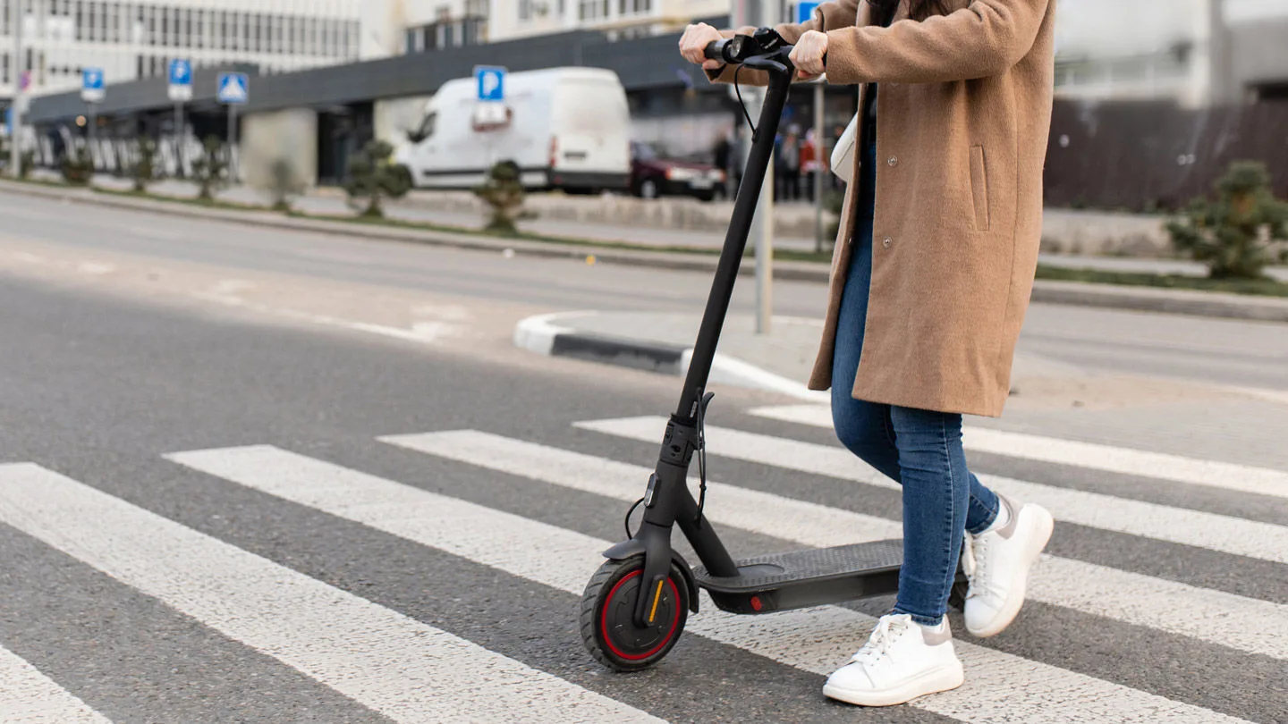 Frau schiebt einen E-Scooter über einen Zebrastreifen