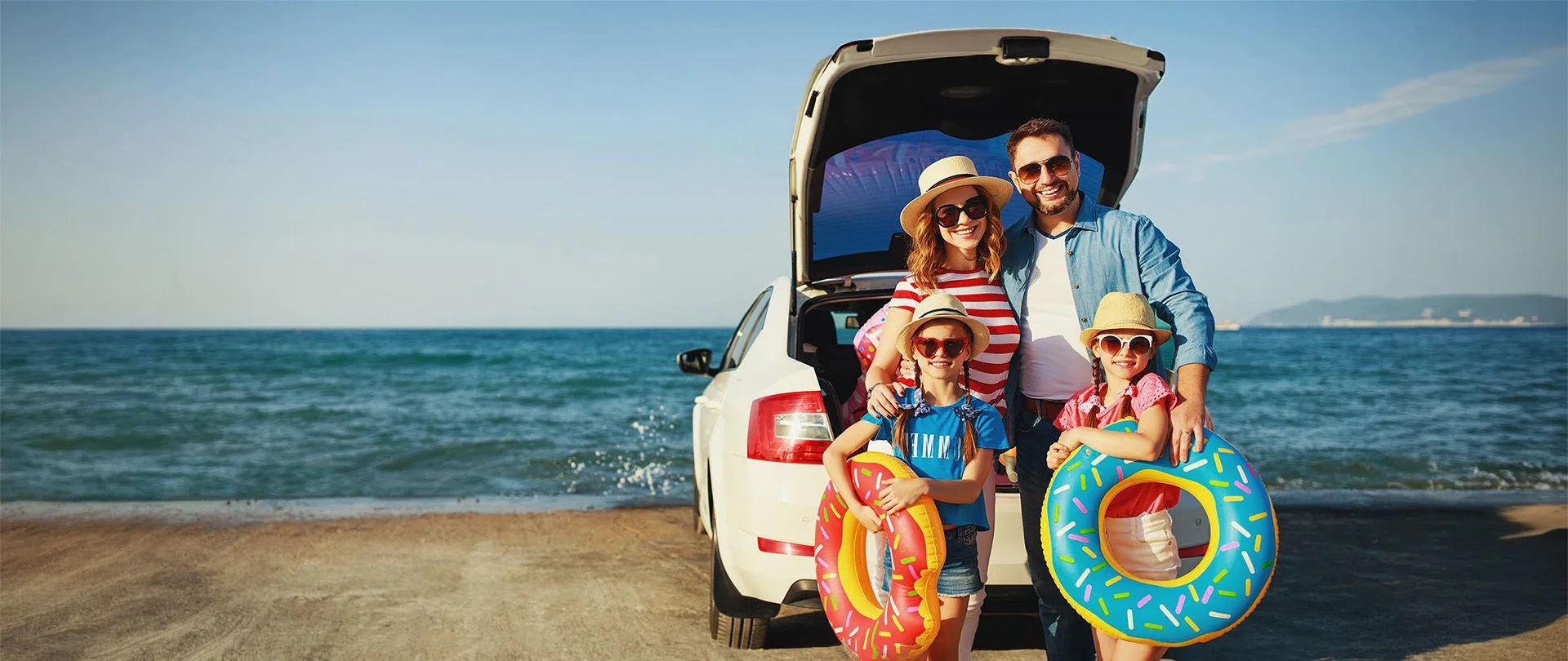 Familie im Sommer am Meer hinter einem Auto