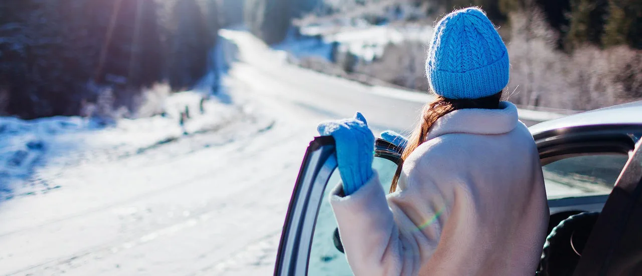Eine Frau steht an einer geöffneten Autotür und schaut auf eine verschneite Strasse