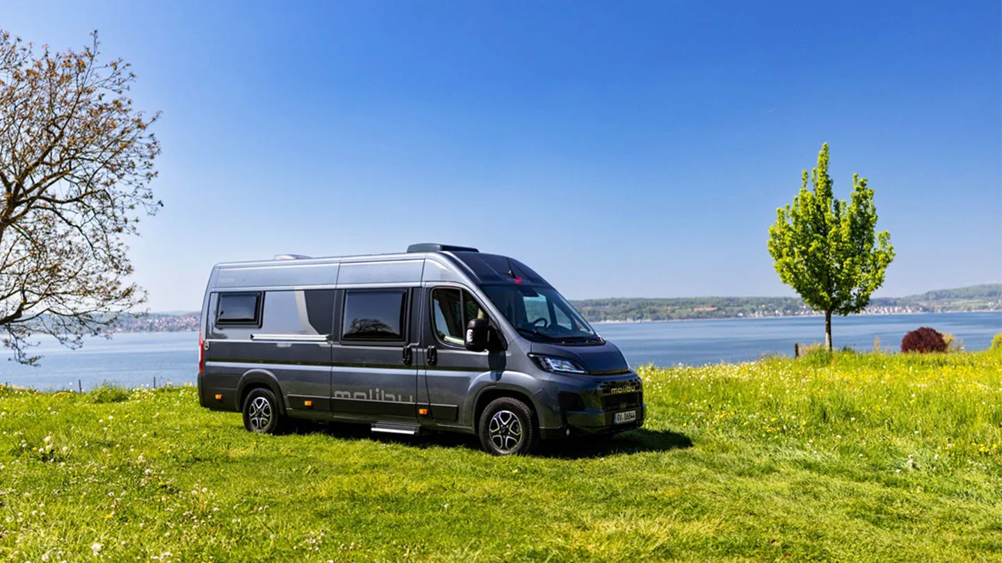 dunkelgrauer Camper steht auf einer Wiese im Hintergrund sieht man einen See