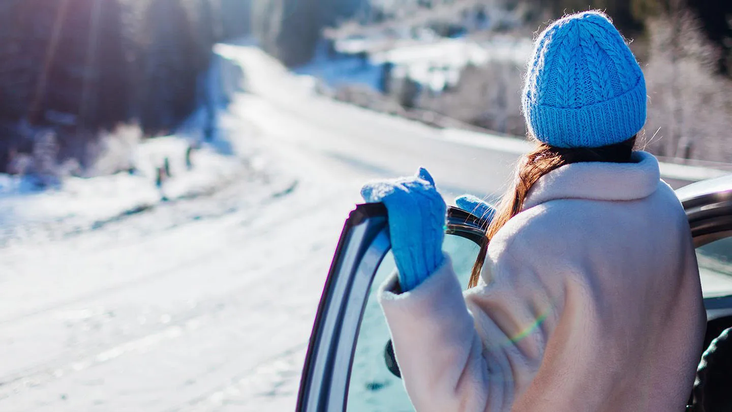 Eine Frau steht an einer geöffneten Autotür und schaut auf eine verschneite Straße