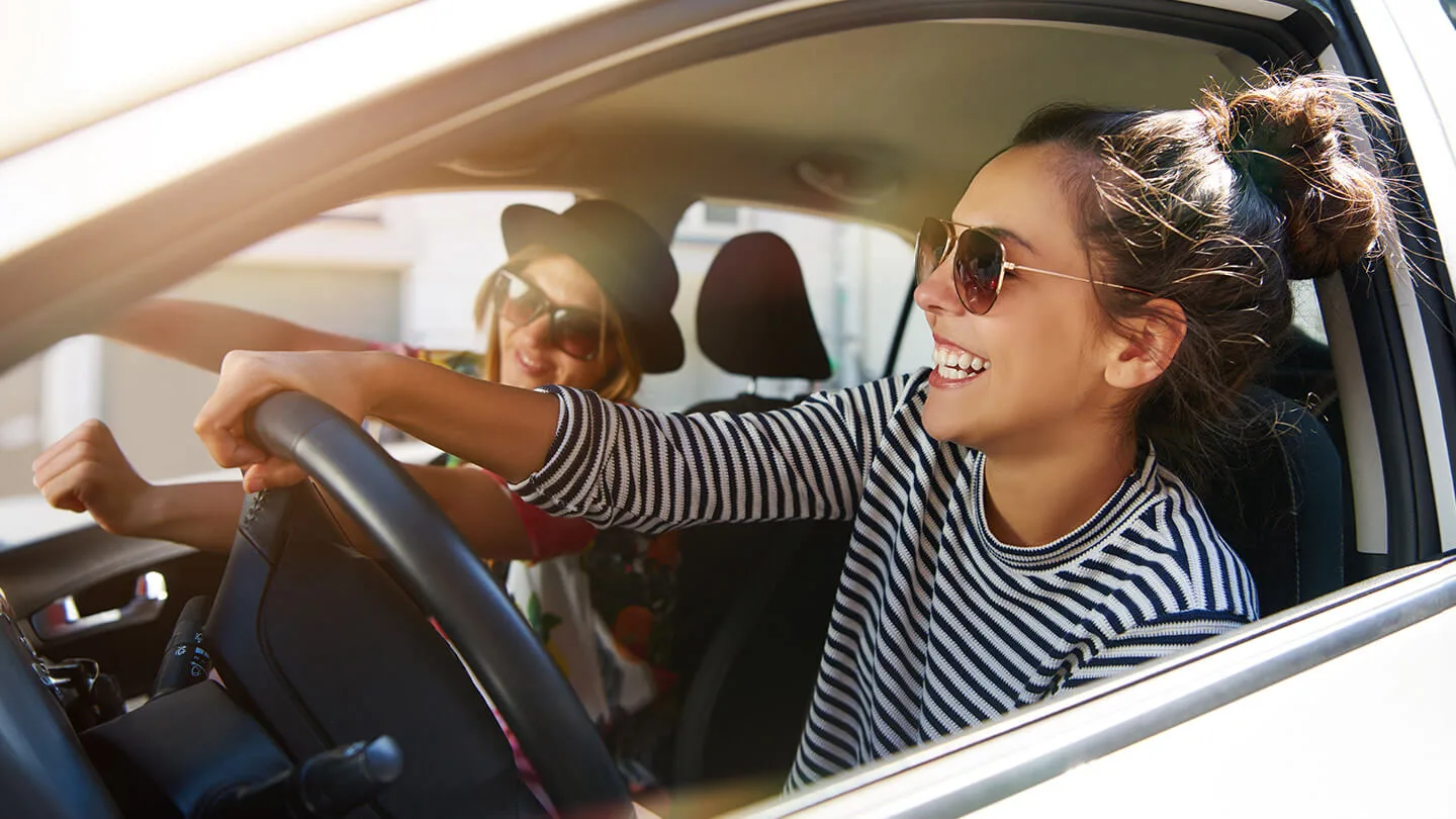 Junge Frau lachend im Auto am Steuer