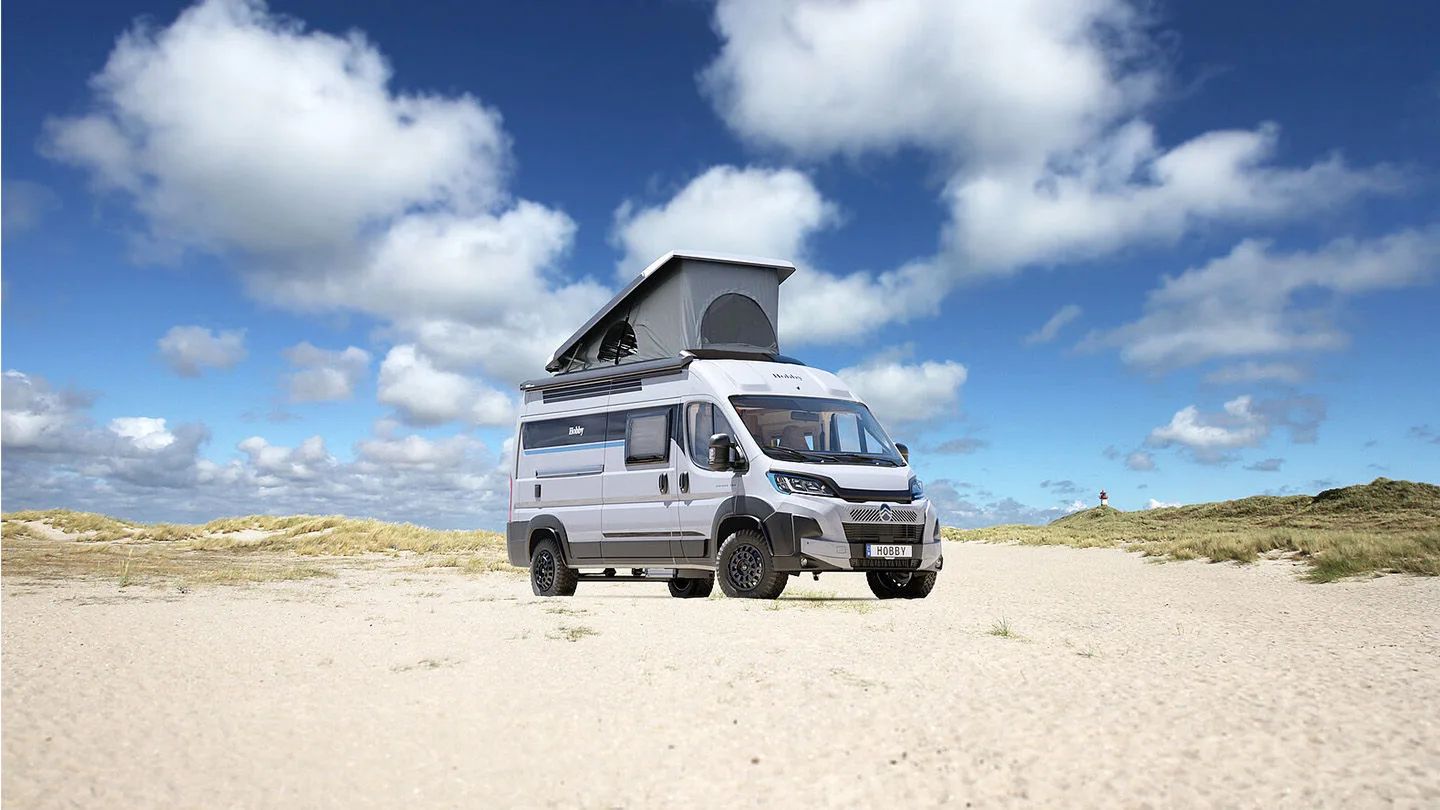 türkisfarbener Campervan von VW steht im Sand