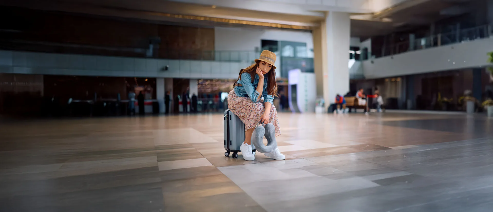 Eine Frau sitzt niedergeschlagen am Flughafen auf ihrem Koffer, ihr Freund ist kurz vor der Reise krank geworden.